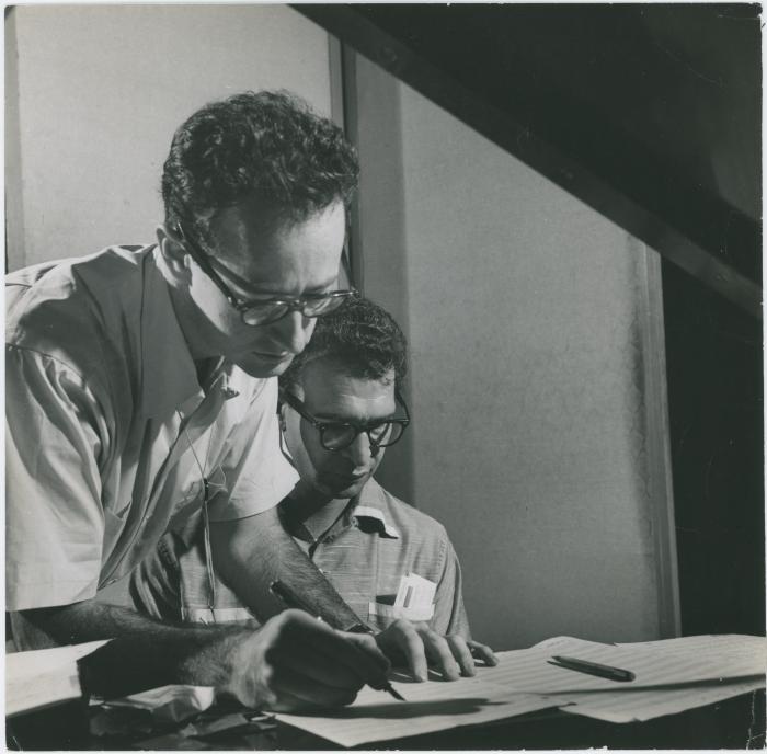 Dave Brubeck at piano, Paul Desmond standing at piano writing