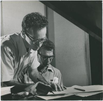 Dave Brubeck at piano, Paul Desmond standing at piano writing