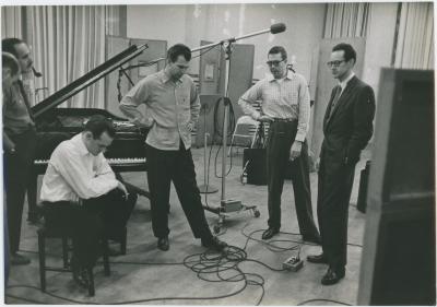 George Avakian and Fred Plant (smoking pipe, Columbia producer and recording engineer), with Norman Bates (seated), Dave Brubeck, Joe Morello, and Paul Desmond listening to playback #1 (New York City, New York [?])