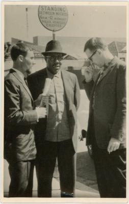 Mike Wilson, Eugene Wright and Joe Morello standing in front of "Standing Between Notices" sign (Sydney, Australia)