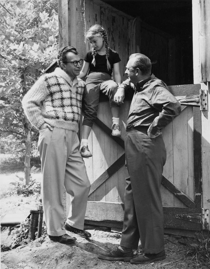 Walter Cronkite and Dave Brubeck standing at the barn door while Catherine Brubeck perches between them during filming of an episode of the CBS television show "The 20th Century" at Dave Brubeck's home (Wilton, Connecticut)